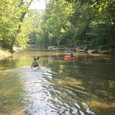 people in kayaks floating down creek