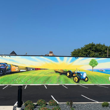 mural painted on side of building with train lake and tractor