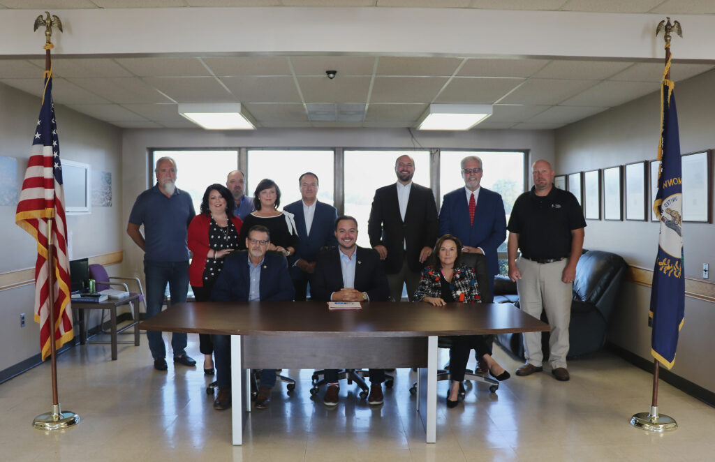 Group of people sitting at and standing behind table with Kentucky and American flags