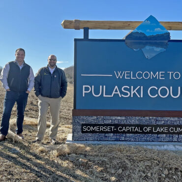 Three men standing to the left of a sign that says Welcome to Pulaski County