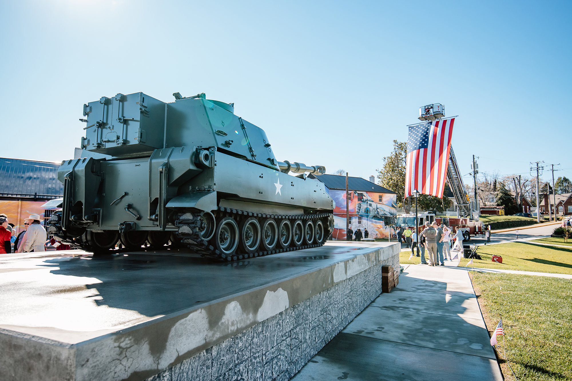 military artillery vehicle on top of a concrete stage with an American flag high on a fire truck in the background