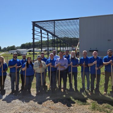 A group of people standing in front of a manufacturing facility under construction.