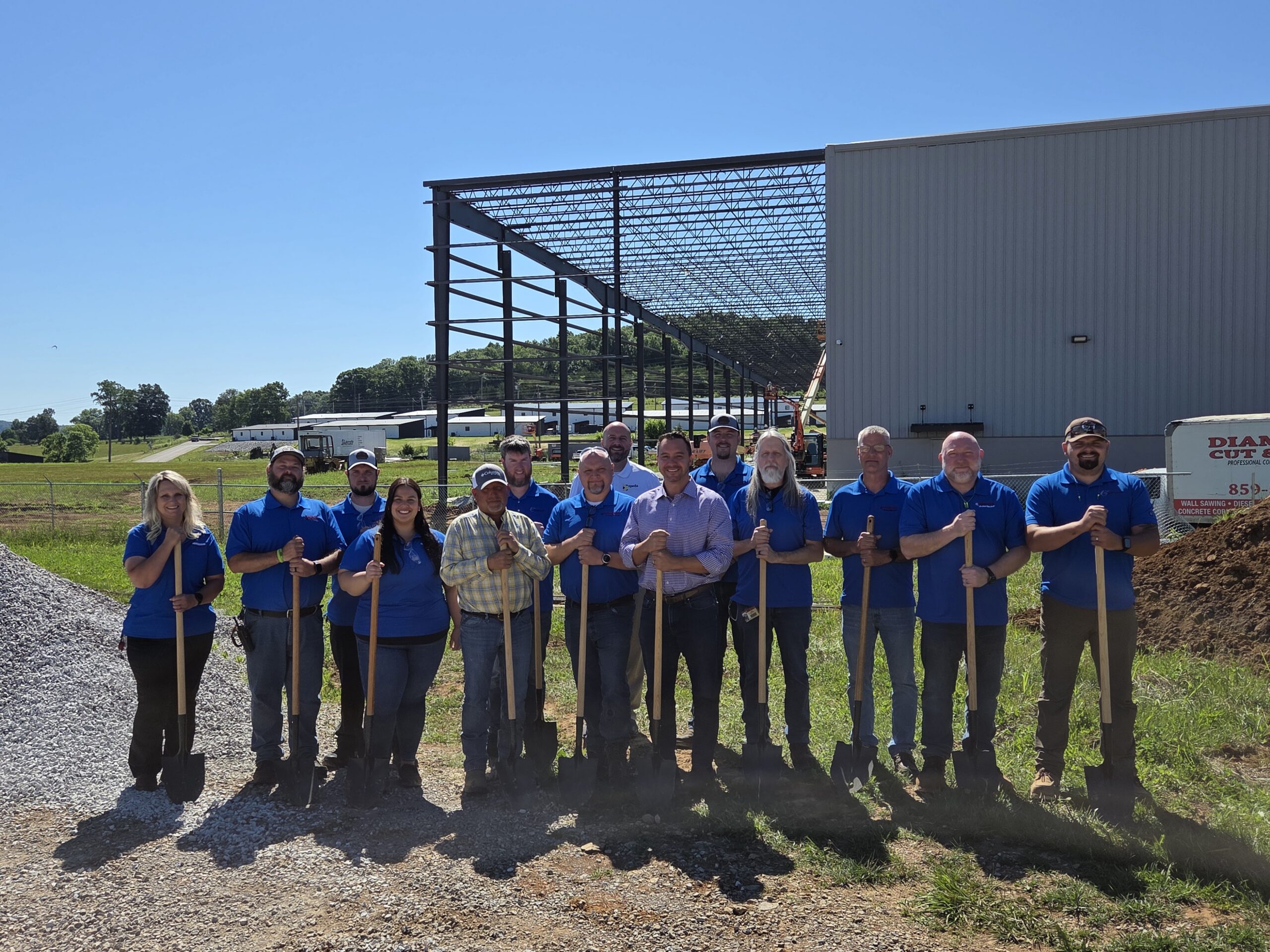 A group of people standing in front of a manufacturing facility under construction.